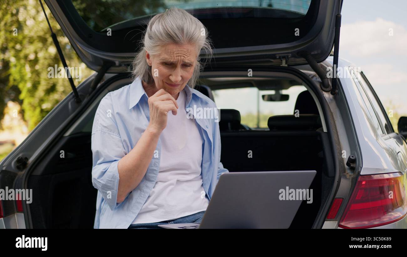 Confus bouleversé caucasien mature femme âgée femme âgée freelance utilisateur SIT voiture coffre d'automobile travaillant en ligne connexion d'ordinateur portable Banque D'Images