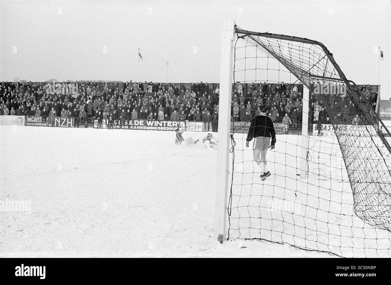 RCH - Ajax, Football, 17-02-1963 Whizgle News, Dutch Desk, pays-Bas, 1950-2000 Un groupe de joueurs se bat dans un match de football enneigé, tandis qu'une foule nombreuse regarde attentivement depuis les tribunes, entouré de paysages hivernaux. Banque D'Images