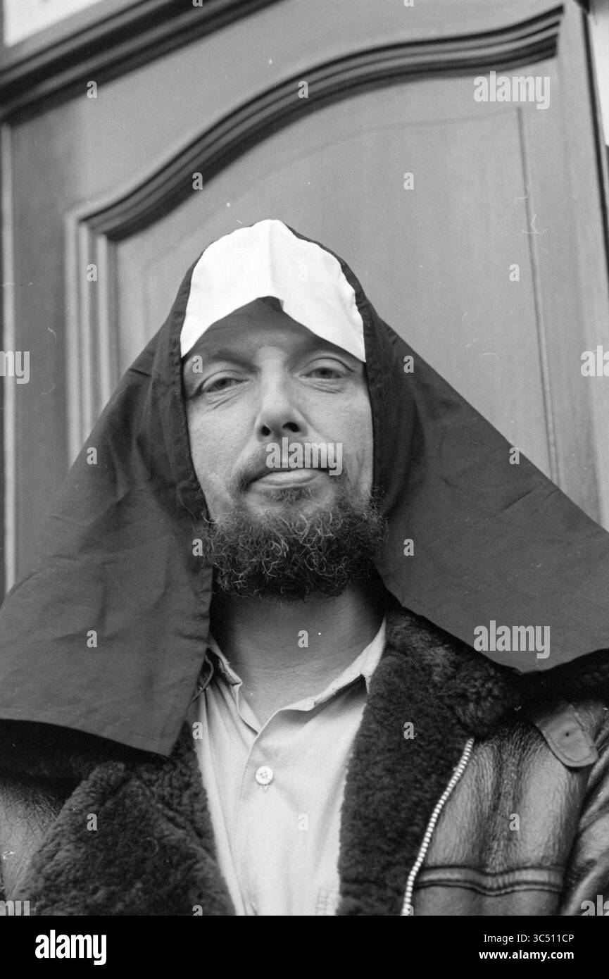 Lennart Nijgh en tant que nonne, écrivains, 16-11-1987 Whizgle News, Dutch Desk, pays-Bas, 1950-2000 Un homme à la barbe porte un couvre-chef qui ressemble à une habitude religieuse, associé à une veste en cuir. Il se tient confiant devant une porte en bois ornée, dégageant une présence unique et intrigante. Banque D'Images