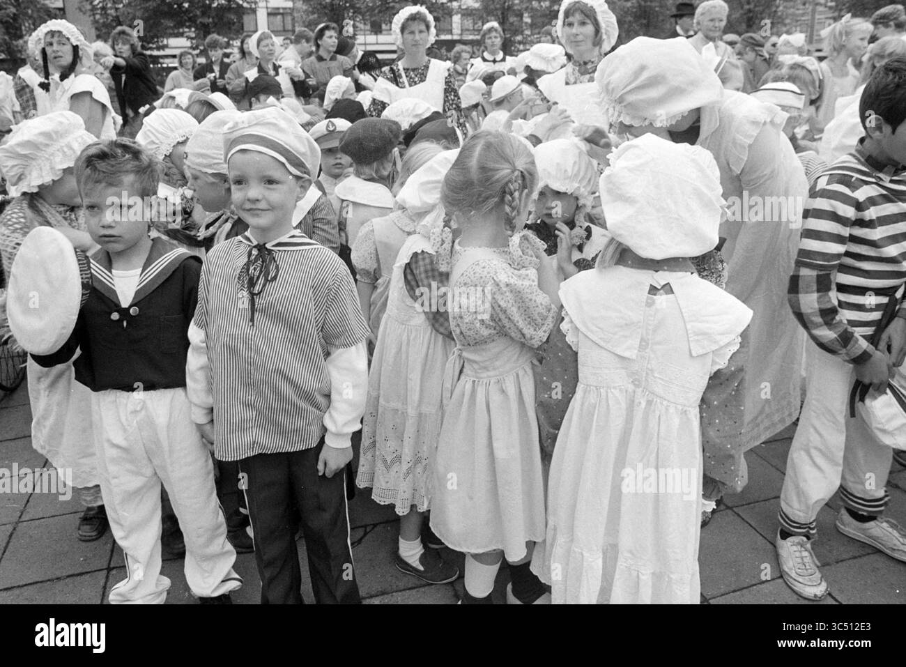 OT and sien parade Plesmanplein, parades, Haarlem, Plesmanplein, pays-Bas, 25-06-1987 Whizgle News, Dutch Desk, pays-Bas, 1950-2000 Un groupe d'enfants vêtus de vêtements vintage, y compris des tenues de marins et des robes traditionnelles, se réunit dans un cadre animé en plein air. Certains enfants sourient tandis que d’autres semblent plus sérieux, mettant en valeur une gamme d’émotions lors d’un événement festif. Des adultes dans une tenue similaire les entourent, créant un sentiment de communauté et de célébration. Banque D'Images