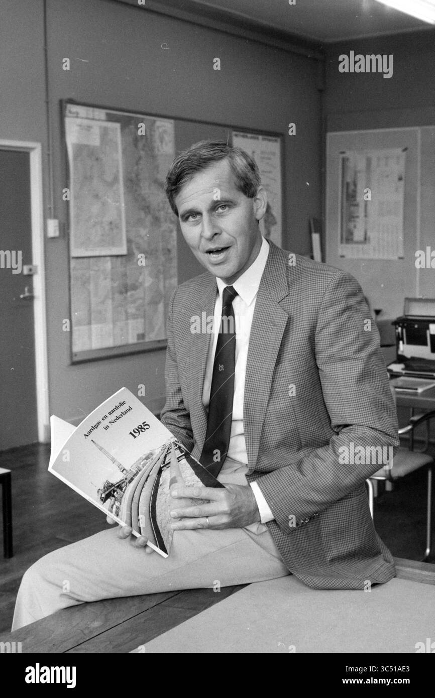 M. Montford Geological Survey, Geology, 02-09-1986 Whizgle News, Dutch Desk, pays-Bas, 1950-2000 Un homme bien habillé est assis à un bureau dans un bureau, tenant une publication intitulée '1975'. Il semble être engagé dans la conversation, discutant peut-être du contenu du livre, tandis que des cartes ornent les murs en arrière-plan. Banque D'Images