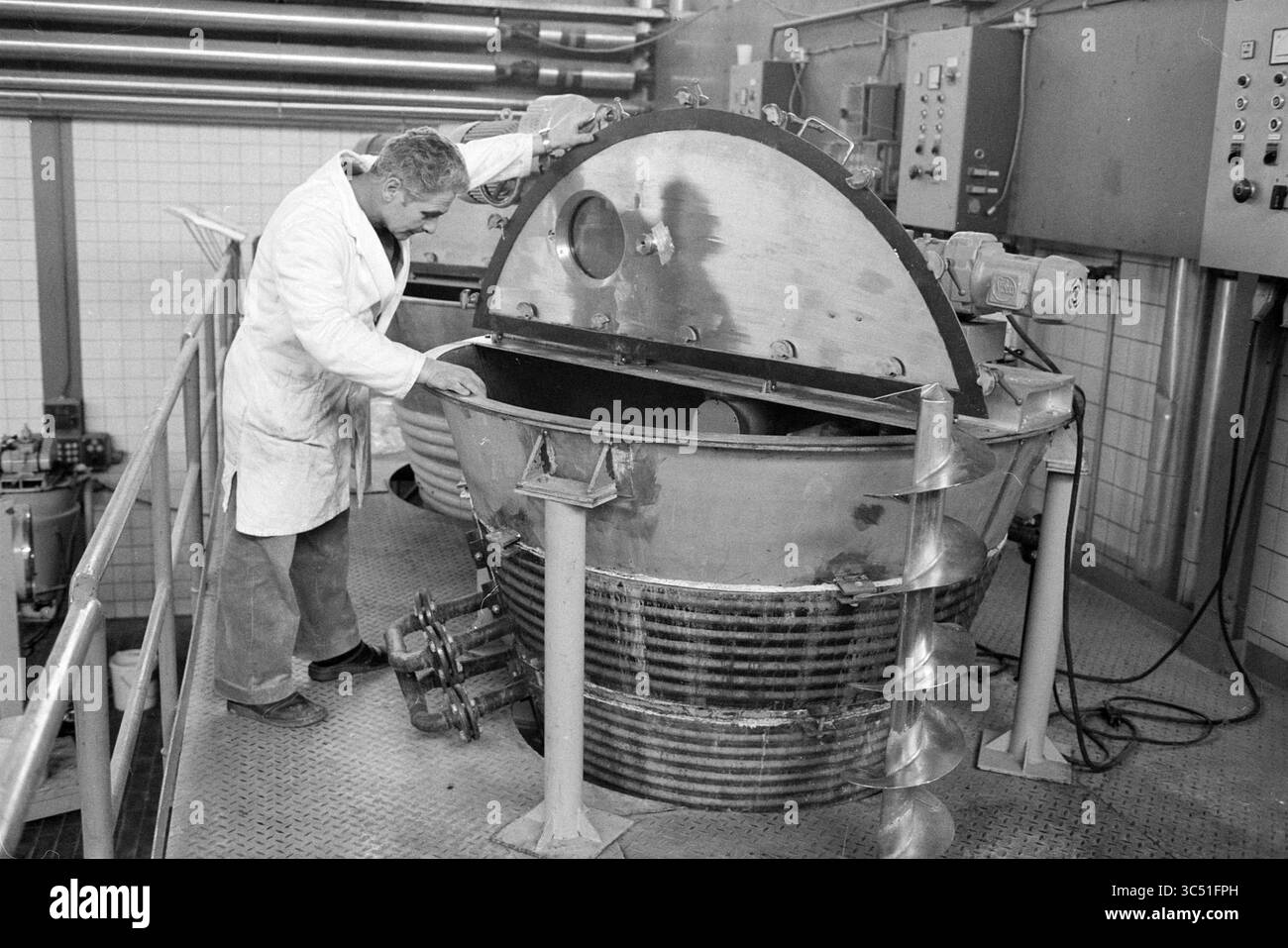 FA. Nautamix, H'lem, usines, fabrication, ateliers, Haarlem, pays-Bas, 26-03-1980 Whizgle News, Dutch Desk, pays-Bas, 1950-2000 Un scientifique portant une blouse de laboratoire inspecte un grand appareil cylindrique, examinant soigneusement son intérieur, entouré d'équipements industriels et de panneaux de commande. Banque D'Images