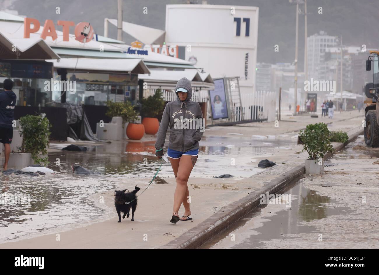 29 juillet 2025, Rio de Janeiro, Rio de Janeiro, Brésil : une jeune femme marche avec son chien le long d'une avenue Delfim Moreira inondée, alors que des équipes de nettoyage municipales de Rio de Janeiro de Comlurb ont été dépêchées pour nettoyer les suites d'une puissante tempête hivernale qui a envoyé des vagues de l'océan déferler sur la plage lors d'un rare événement d'onde de tempête, inondant la promenade Leblon et l'avenue Delfim Moreira. La vague violente a causé d'importants dommages à plusieurs kiosques en bord de mer et dispersé des débris sur la côte normalement animée. (Crédit image : © Bob Karp/ZUMA Press Wire) USAGE ÉDITORIAL SEULEMENT ! Non destiné à des fins commerciales Banque D'Images