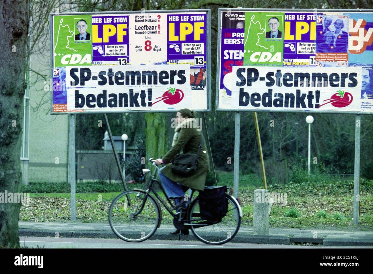 Election Board SP, Bloemendaal, Bloemendaal, 11-03-2003 Whizgle News, Dutch Desk, pays-Bas, 1950-2000 Une personne passe à vélo devant une série de grandes affiches de campagne politique affichant divers logos et messages de parti, soulignant l'importance de la participation des électeurs. La scène se déroule sur fond urbain, avec des arbres bordant la rue. Banque D'Images