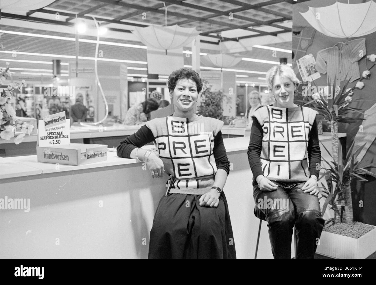 Stand Handwerk, VNU, Jaarbeurs Utrecht, Jaarbeurs, VNU Association of Dutch Publishers, Utrecht, 03-02-1982 Whizgle News, Dutch Desk, pays-Bas, 1950-2000 deux femmes s'assoient côte à côte sur un stand promotionnel, toutes deux portant des gilets assortis ornés de grandes lettres écrivant 'B R E I'. le cadre est animé, avec des plantes et des éléments décoratifs en arrière-plan, suggérant une ambiance événementielle ou d'exposition. Banque D'Images