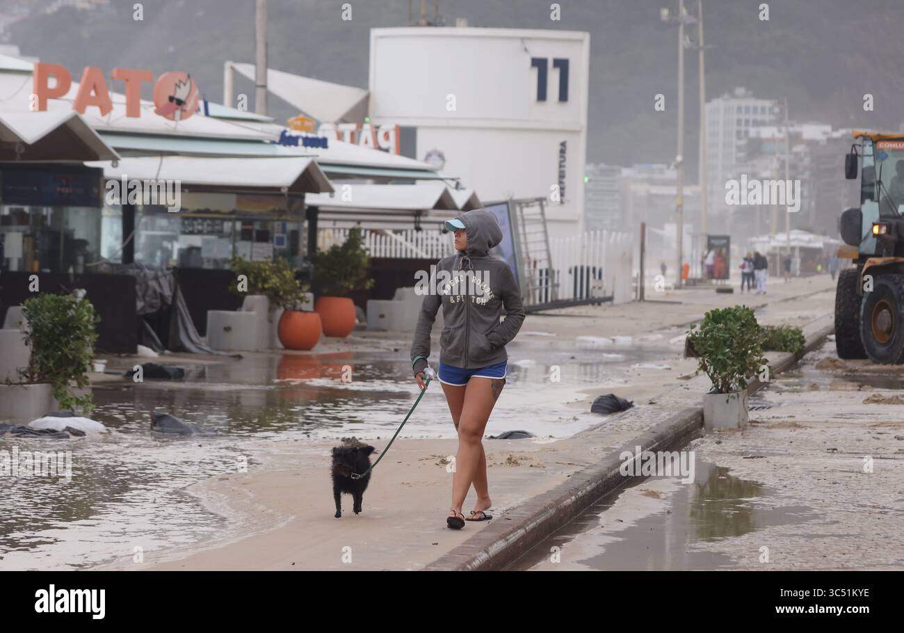 29 juillet 2025, Rio de Janeiro, Rio de Janeiro, Brésil : une jeune femme marche avec son chien le long d'une avenue Delfim Moreira inondée, alors que des équipes de nettoyage municipales de Rio de Janeiro de Comlurb ont été dépêchées pour nettoyer les suites d'une puissante tempête hivernale qui a envoyé des vagues de l'océan déferler sur la plage lors d'un rare événement d'onde de tempête, inondant la promenade Leblon et l'avenue Delfim Moreira. La vague violente a causé d'importants dommages à plusieurs kiosques en bord de mer et dispersé des débris sur la côte normalement animée. (Crédit image : © Bob Karp/ZUMA Press Wire) USAGE ÉDITORIAL SEULEMENT ! Non destiné à des fins commerciales Banque D'Images