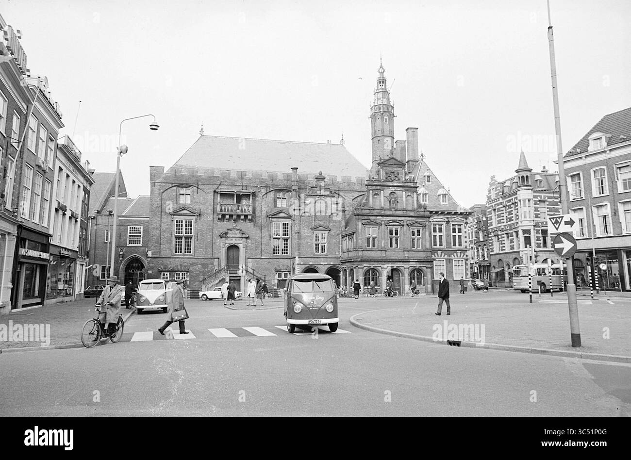 Hôtel de ville avec trafic sur Grote Markt, Haarlem, Grote Markt, pays-Bas, 00-00-1965 Whizgle News, Dutch Desk, pays-Bas, 1950-2000 Une place animée dispose d'un bâtiment historique avec des détails architecturaux, tandis que les gens naviguent dans la rue, certains à pied et d'autres à vélo. Un van emblématique est garé à proximité, ajoutant une touche de nostalgie à la scène. Banque D'Images