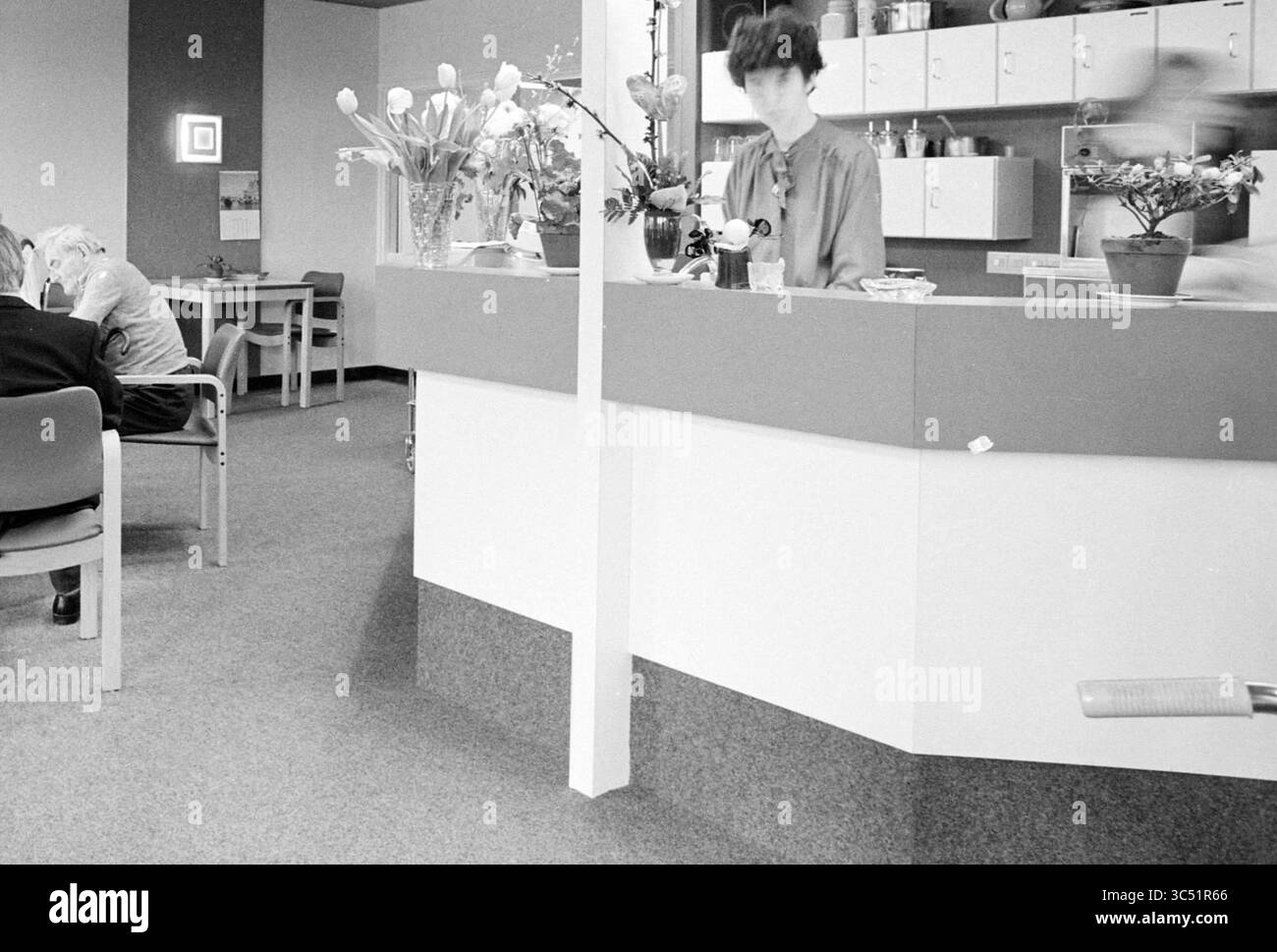 Rapport sur la maison de soins Overspaarne, hôpitaux, Haarlem, pays-Bas, 13-03-1980 Whizgle News, Dutch Desk, pays-Bas, 1950-2000 Un espace de réception doté d'un comptoir orné de fleurs et de plantes, où un membre du personnel s'occupe des tâches, tandis que les clients sont assis à proximité dans une salle d'attente. L'ambiance est calme et accueillante. Banque D'Images