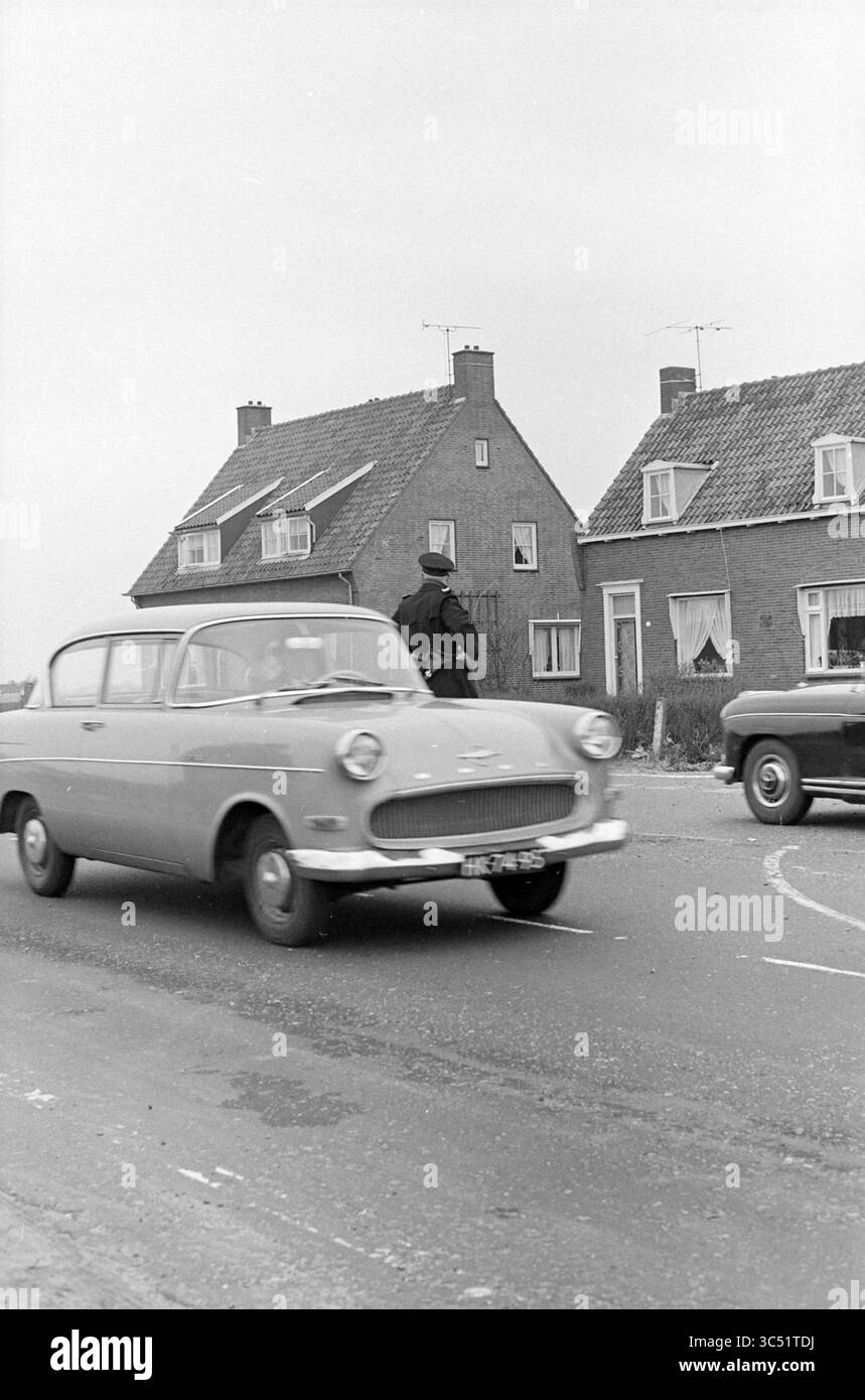 La police réglemente la circulation des visiteurs aux champs de bulbes de fleurs Whizgle News, Dutch Desk, pays-Bas, 1950-2000 Une voiture classique passe devant une rue résidentielle, où une personne peut être vue debout près d'une maison avec des fenêtres et des toits distinctifs. Un autre véhicule vintage est visible en arrière-plan, contribuant à l’atmosphère nostalgique de la scène. Banque D'Images