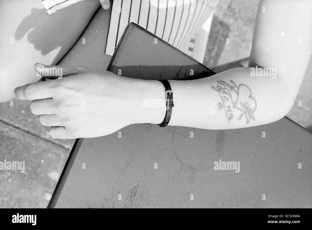 Conversation sur la plage tatouages de la CMI, 02-07-1991 Whizgle News, Dutch Desk, pays-Bas, 1950-2000 gros plan d'un bras au repos désinvolte orné d'un tatouage, reposant sur une table, montrant une montre au poignet. Le cadre évoque une atmosphère détendue et décontractée. Banque D'Images