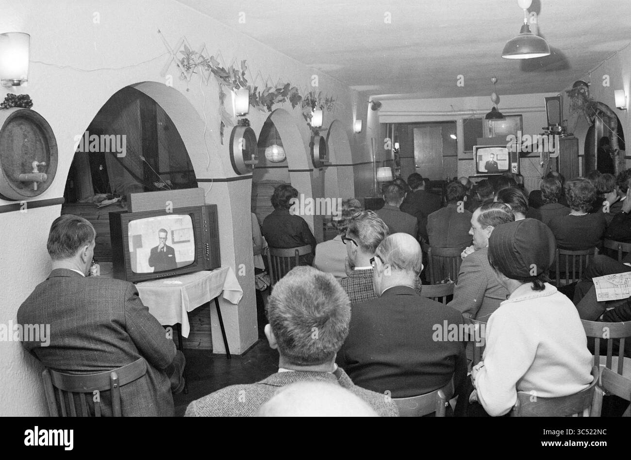 Teach-In Noise pollution Schiphol, Schiphol, 02-11-1967 Whizgle News, Dutch Desk, pays-Bas, 1950-2000 Un groupe de personnes assis dans une pièce confortable, regardant attentivement une émission de télévision. Le cadre comprend des portes voûtées, des meubles en bois et un éclairage ambiant, créant une atmosphère de rassemblement et d'expérience partagée. Banque D'Images