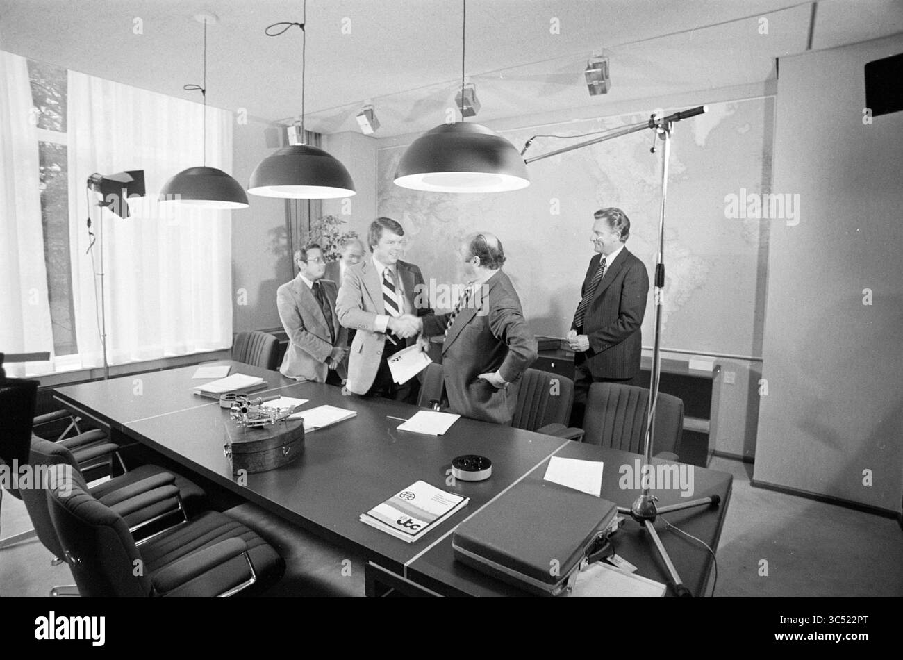 ITC signe un contrat avec Western Oceanic, I.T.C., 02-09-1976 Whizgle News, Dutch Desk, pays-Bas, 1950-2000 Un groupe de quatre hommes en tenue d'affaires sont engagés dans une discussion autour d'une longue table de conférence, l'un d'eux serrant la main et les autres écoutant attentivement. La salle dispose de grands luminaires et d'une carte du monde sur le mur, créant une atmosphère professionnelle. Des papiers et un petit contenant sont placés sur la table, indiquant une réunion ou une négociation officielle. Banque D'Images