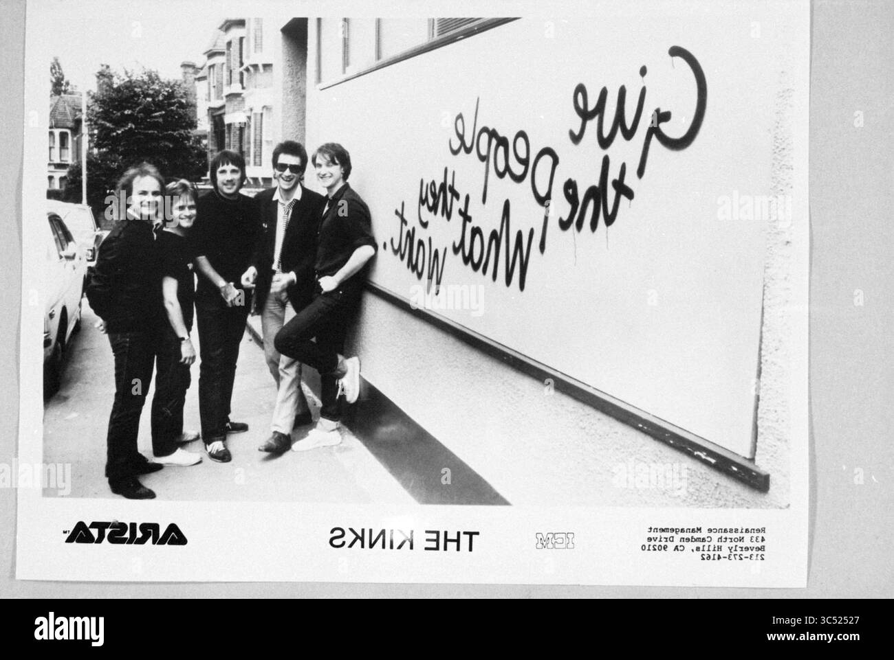 Photo du groupe photo pop The Kinks, 00-09-1981 Whizgle News, Dutch Desk, pays-Bas, 1950-2000 Un groupe de cinq personnes se tient ensemble, posant avec confiance devant un mur avec un message ludique qui suggère un sentiment de camaraderie et de légèreté. Le cadre semble urbain, avec des bâtiments en arrière-plan ajoutant à l'atmosphère animée. Banque D'Images