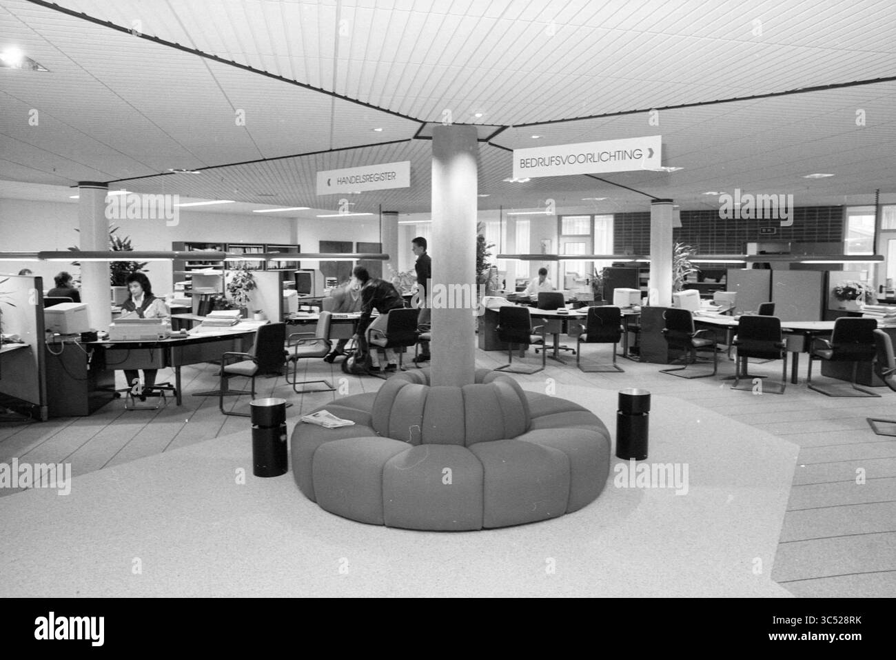 Divers intérieurs et ext. nouvelle construction, Chambre de commerce et usines, 16-11-1987 Whizgle News, Dutch Desk, pays-Bas, 1950-2000 Un environnement de bureau spacieux dispose de postes de travail modernes avec des employés engagés dans diverses tâches. Au centre, un coin salon circulaire distinctif invite à une collaboration décontractée. Les panneaux indiquant les différentes sections du bureau améliorent l'organisation et le flux de travail. Banque D'Images