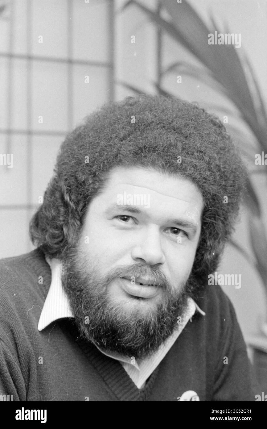 Portrait homme, 00-01-1985 Whizgle News, Dutch Desk, pays-Bas, 1950-2000 Un homme avec une coiffure afro proéminente et une barbe pleine sourit doucement, portant un pull sur une chemise à col. Il semble détendu et accessible, avec une mise au point douce sur une plante en arrière-plan. Banque D'Images Portrait homme, 00-01-1985 Whizgle News, Dutch Desk, pays-Bas, 1950-2000 Un homme avec une coiffure afro proéminente et une barbe pleine sourit doucement, portant un pull sur une chemise à col. Il semble détendu et accessible, avec une mise au point douce sur une plante en arrière-plan. Banque D'Images