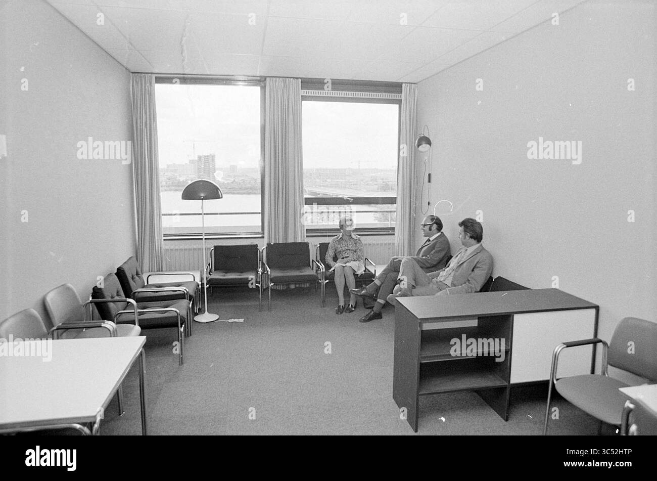 Rapport Diakonessenhuis, Report, 24-07-1973 Whizgle News, Dutch Desk, pays-Bas, 1950-2000 Une salle d'attente minimaliste comprend trois personnes engagées dans la conversation, entourées de meubles simples qui comprennent des chaises et un bureau. De grandes fenêtres offrent une vue sur l'extérieur, ajoutant un sentiment d'ouverture à l'espace. Banque D'Images