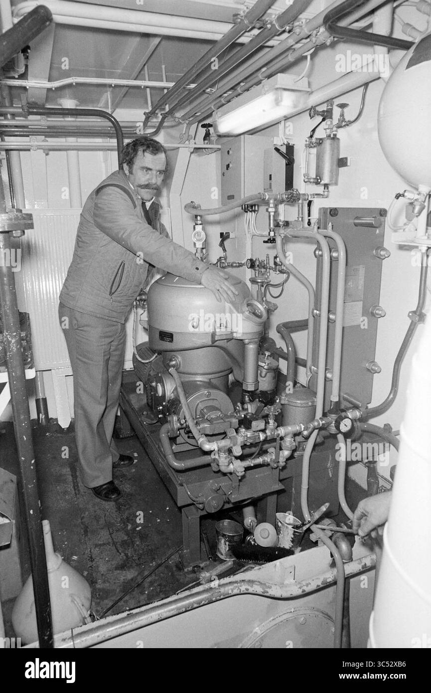 HR Molijn)RIVO) IJm + HR Molijn dans la salle des machines du bateau, construction navale, expédition, 23-01-1981 Whizgle News, Dutch Desk, pays-Bas, 1950-2000 Un technicien se tient à côté d'un assemblage complexe de tuyaux et de machines, ajustant un gros compresseur au cœur d'un système mécanique. L'environnement est industriel, avec des équipements visibles et des panneaux de contrôle autour de lui. Banque D'Images