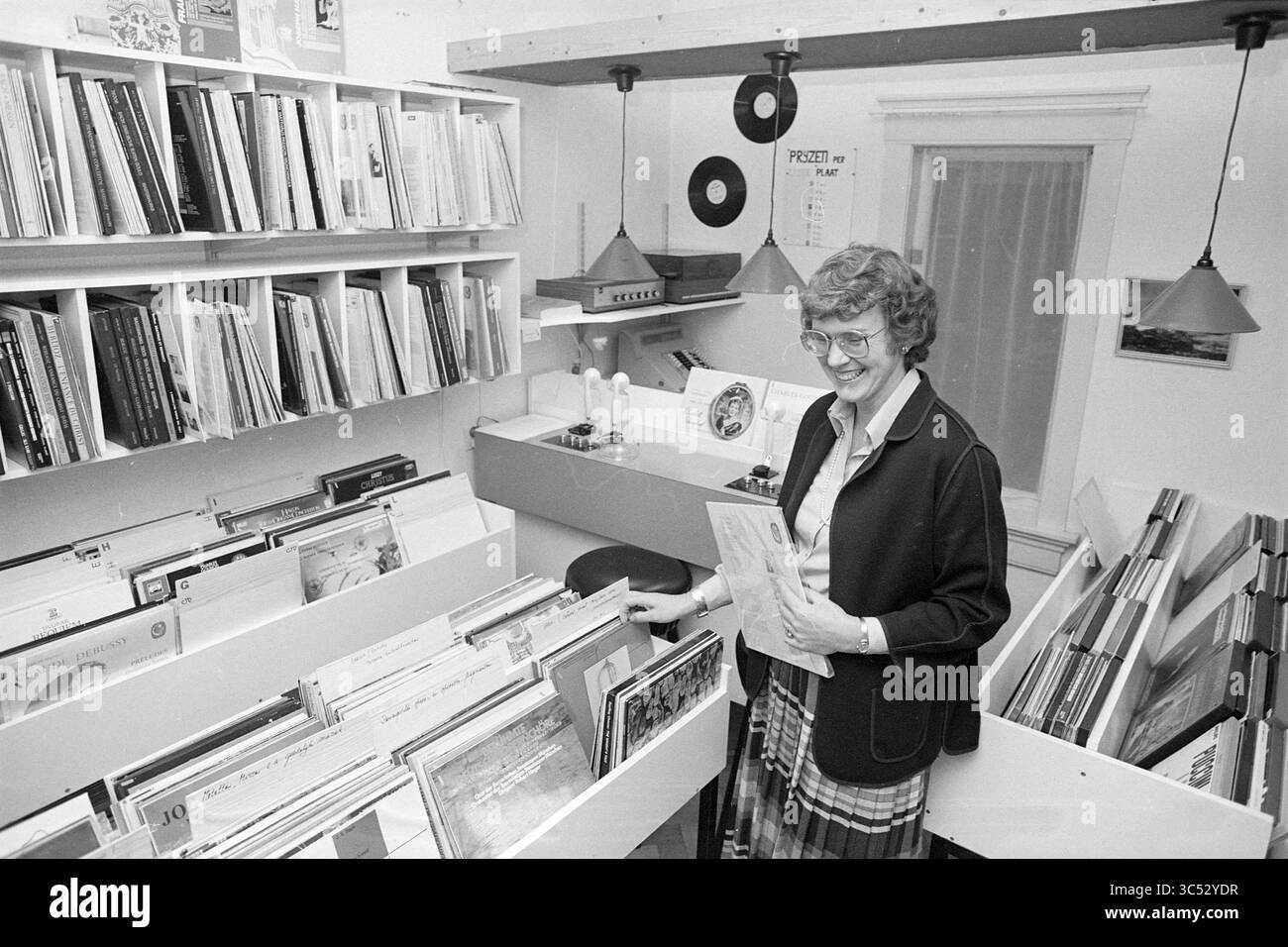 Polyphone 2nd Hand Records Haarlem, Gramophone et maisons de disques, magasins et kiosques, Haarlem, pays-Bas, 05-11-1984 Whizgle News, Dutch Desk, pays-Bas, 1950-2000 Une femme se tient dans un espace confortable rempli d'étagères de disques, souriant alors qu'elle tient un album vinyle. La salle dispose d'un éclairage chaleureux et de disques vintage ornent les murs, créant une atmosphère accueillante pour les amateurs de musique. Banque D'Images