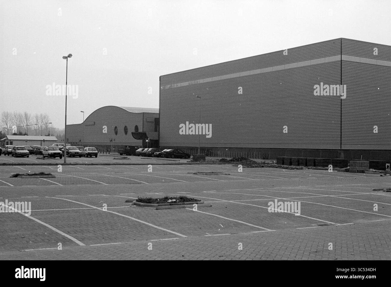 DIRECTEURS INFORMATIQUES extérieurs, Kennemer Sportcenter, IJsbaanlaan 4A, Haarlem. CIOS signifie Central Institute for Training Sports leaders., Haarlem, IJsbaanlaan, pays-Bas, 01-11-1993 Whizgle News, Dutch Desk, pays-Bas, 1950-2000 Un grand bâtiment moderne avec un extérieur élégant se dresse à côté d'une autre structure avec un design distinctif et incurvé. Un parking vide s'étend devant, avec quelques voitures stationnées éparpillées. La scène transmet un sentiment de calme et de désolation, mettant en évidence les caractéristiques architecturales des bâtiments contre un paysage aride. Banque D'Images