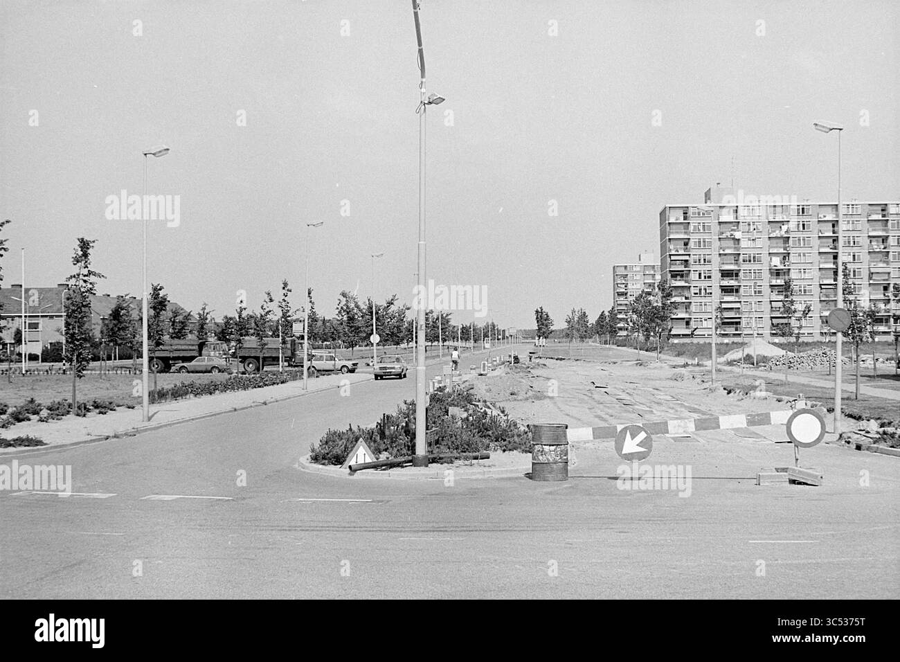 Activités Maerelaan Heemskerk, activités, Heemskerk, Maerelaan, 24-06-1974 Whizgle News, Dutch Desk, pays-Bas, 1950-2000 Un carrefour calme présente une route circulaire avec une barrière et des panneaux de signalisation, entourée d'arbres clairsemés et d'un immeuble d'appartements en arrière-plan. Quelques véhicules sont visibles, ainsi que des activités de construction dans la région. Banque D'Images