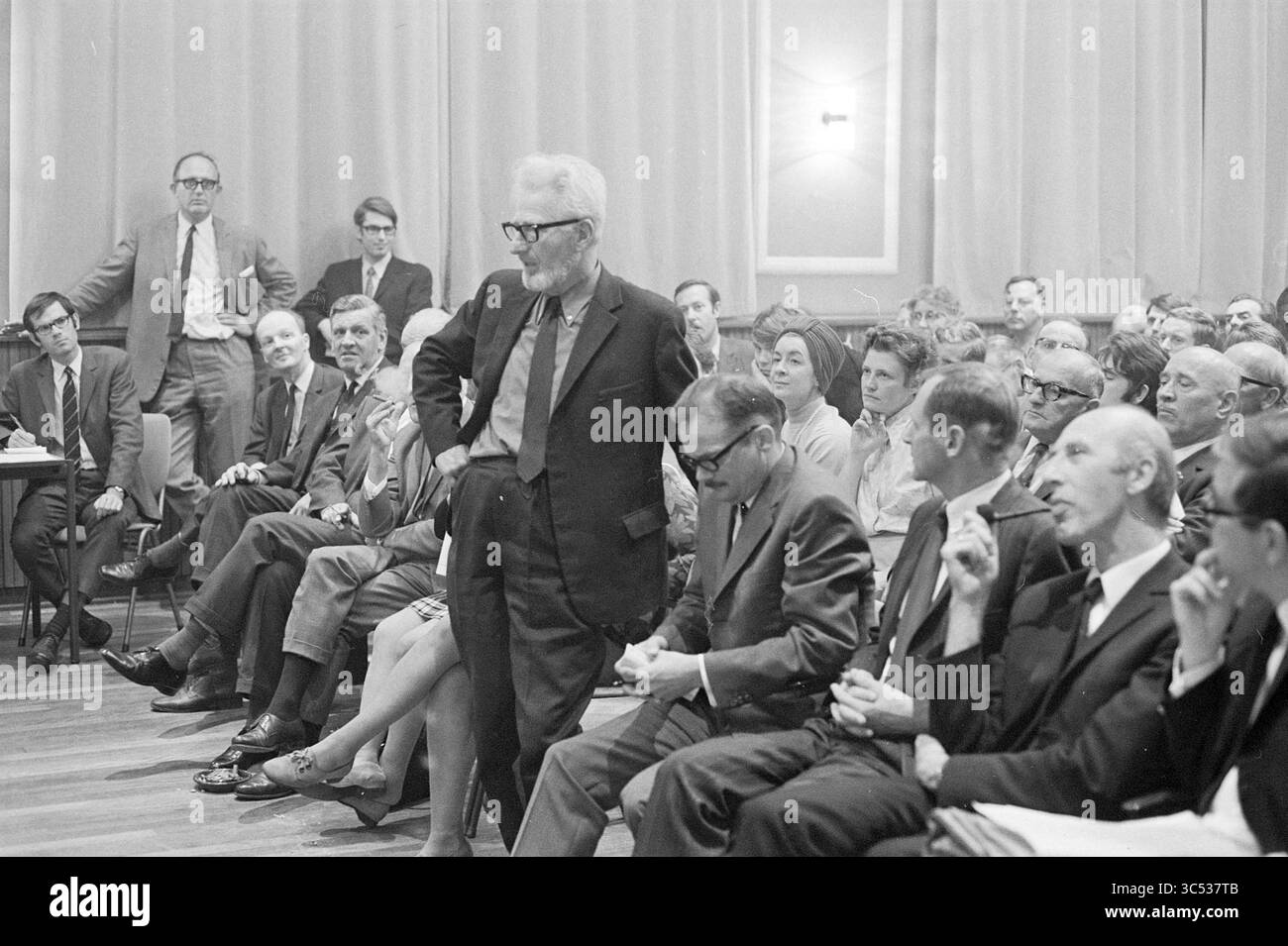 Centre-ville Teach-In, réunions, 24-10-1969 Whizgle News, Dutch Desk, pays-Bas, 1950-2000 Un groupe d'hommes et de femmes s'assoient dans un cadre formel, écoutant attentivement comme un individu se tient au centre, engageant le public avec un comportement confiant. L'atmosphère suggère une discussion ou un débat sérieux, avec diverses expressions reflétant l'intérêt et la contemplation parmi les participants. Banque D'Images