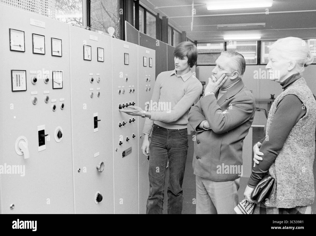 École de pêche ouverte, IJmuiden, Pêches et autres, poissonniers, pêche, IJmuiden, pays-Bas, 10-11-1979 Whizgle News, Dutch Desk, pays-Bas, 1950-2000 Un jeune homme fait des gestes vers un panneau de commande rempli de cadrans et de commutateurs, tandis que deux personnes plus âgées écoutent attentivement, profondément dans la pensée. Le cadre semble être une installation technique ou d'ingénierie, mettant l'accent sur un moment d'instruction ou de démonstration. Banque D'Images