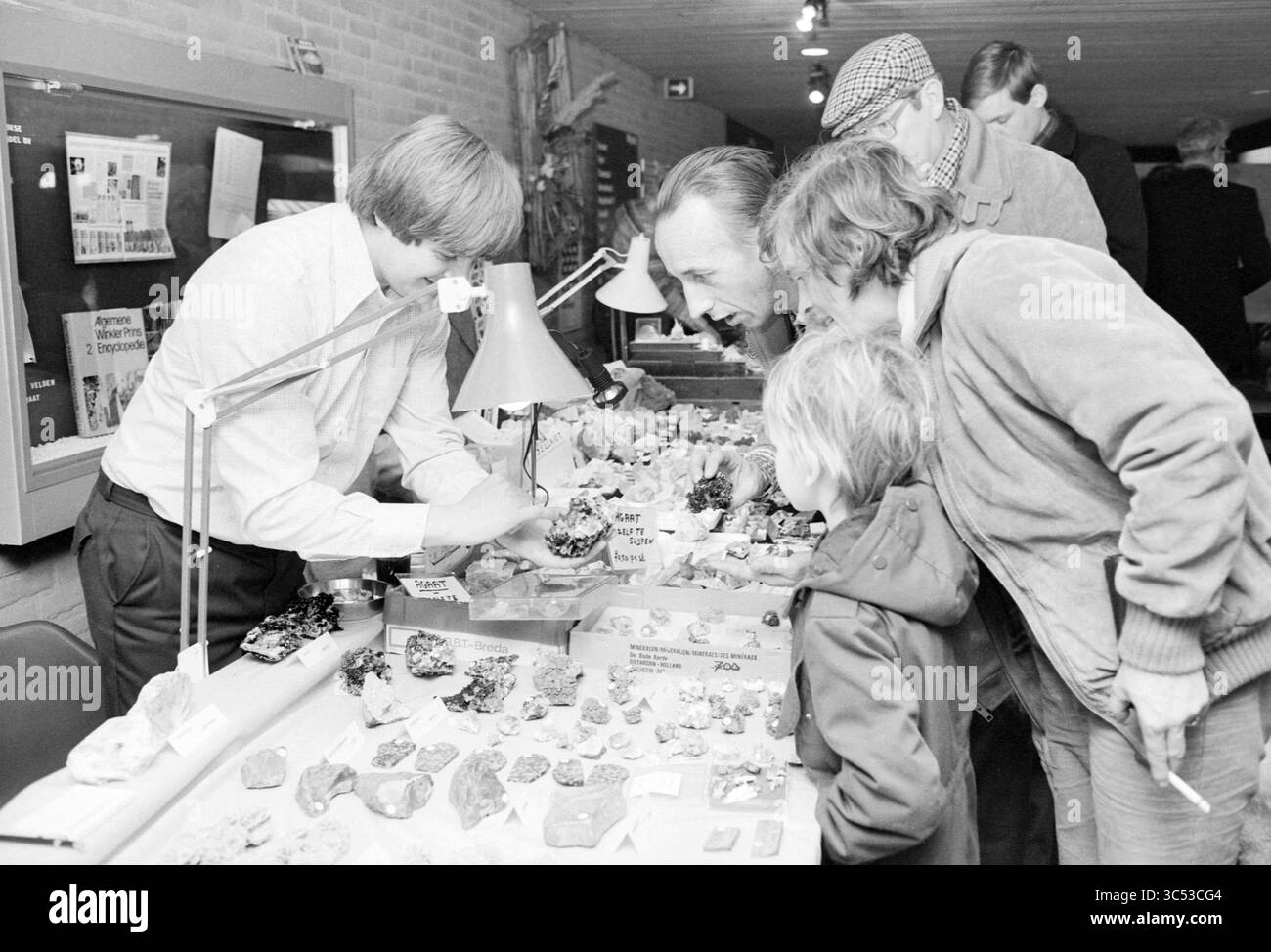 Exposition dans une salle de sport (stand avec minéraux), 03-02-1979 Whizgle News, Dutch Desk, pays-Bas, 1950-2000 Un groupe de personnes, dont un homme adulte et un enfant, observe et discute d'une exposition de diverses roches et minéraux colorés lors d'un événement communautaire. L'ambiance est animée, avec d'autres naviguant à proximité. Banque D'Images Exposition dans une salle de sport (stand avec minéraux), 03-02-1979 Whizgle News, Dutch Desk, pays-Bas, 1950-2000 Un groupe de personnes, dont un homme adulte et un enfant, observe et discute d'une exposition de diverses roches et minéraux colorés lors d'un événement communautaire. L'ambiance est animée, avec d'autres naviguant à proximité. Banque D'Images