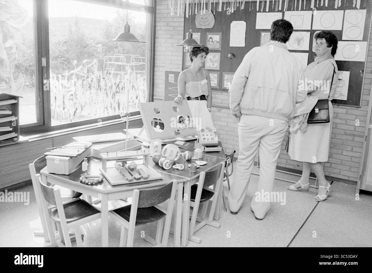 Centre de garderie de Luchtballon, Heemskerk, enfants, enfants, maisons pour enfants, fête d'enfants, enfants, Heemskerk, 19-06-1986 Whizgle News, Dutch Desk, pays-Bas, 1950-2000 Un groupe de trois personnes engage une conversation dans une salle de classe remplie de matériel pédagogique. Les murs décorés de couleurs vives exposent des œuvres d'art pour enfants, tandis qu'une table à proximité est encombrée de divers jouets et outils d'apprentissage. L'atmosphère suggère un environnement axé sur l'apprentissage et la créativité. Banque D'Images