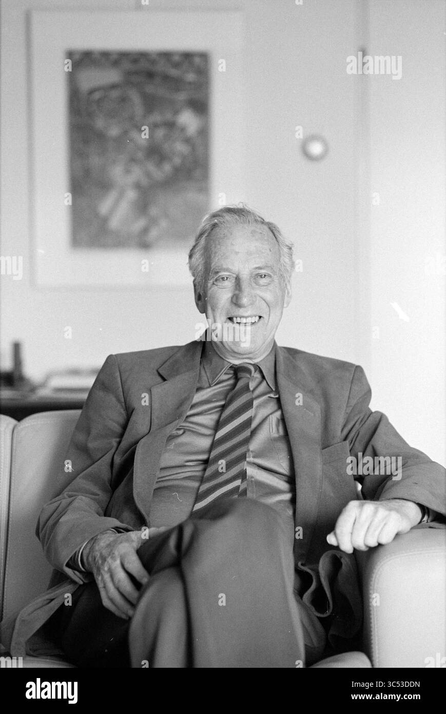 Ancien conseiller Geluk Hazepaterslaan, échevins, Haarlem, Hazepaterslaan, pays-Bas, 15-02-1988 Whizgle News, Dutch Desk, pays-Bas, 1950-2000 un homme âgé s'assoit confortablement dans une chaise, vêtu d'un costume formel avec une cravate, souriant chaleureusement. Le fond présente des tissus d'ameublement et une œuvre d'art sur le mur, créant une atmosphère détendue. Banque D'Images