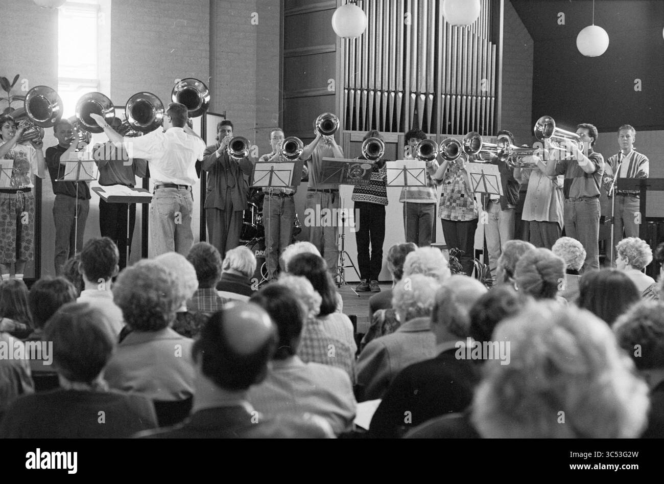 Café concert, Fidelishof, IJmuiden, IJmuiden, Fidelishof, pays-Bas, 13-03-1993 Whizgle News, Dutch Desk, pays-Bas, 1950-2000 Un ensemble diversifié de musiciens se produit sur scène, jouant un éventail de tubas et d'autres instruments, tandis qu'un public attentif écoute au premier plan. Le décor comprend un grand orgue à pipe en arrière-plan et un éclairage doux provenant de luminaires suspendus. Banque D'Images