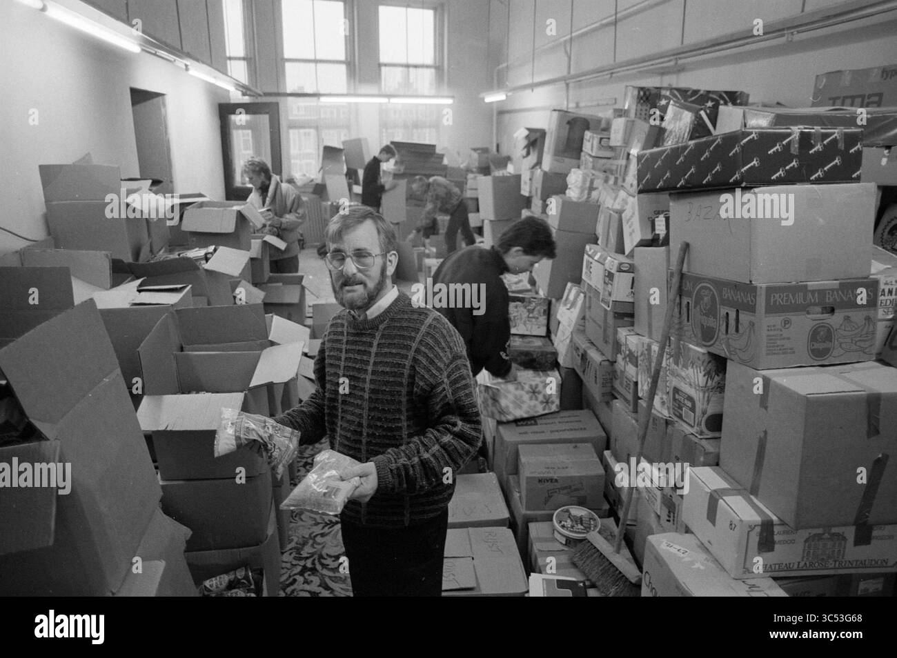 Collecter de la nourriture pour les moins fortunés, 02-01-1990 Whizgle News, Dutch Desk, pays-Bas, 1950-2000 Une salle animée remplie de boîtes en carton empilées où les individus trient et organisent des dons, créant un sentiment d'effort communautaire et de collaboration. Banque D'Images