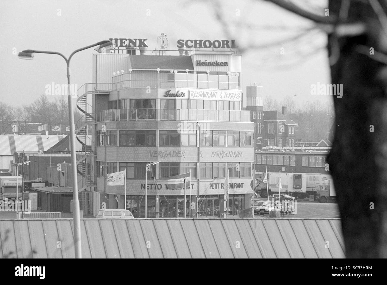 Extérieur Henk Schoorl, IJmuiden, IJmuiden, Halkade, pays-Bas, 05-02-1995 Whizgle News, Dutch Desk, pays-Bas, 1950-2000 Un bâtiment à plusieurs niveaux dispose d'un restaurant et d'un bar, affichant bien en vue des enseignes pour Heineken et diverses options de restauration. Autour de la structure se trouvent des véhicules et des établissements commerciaux, créant une atmosphère animée. Banque D'Images