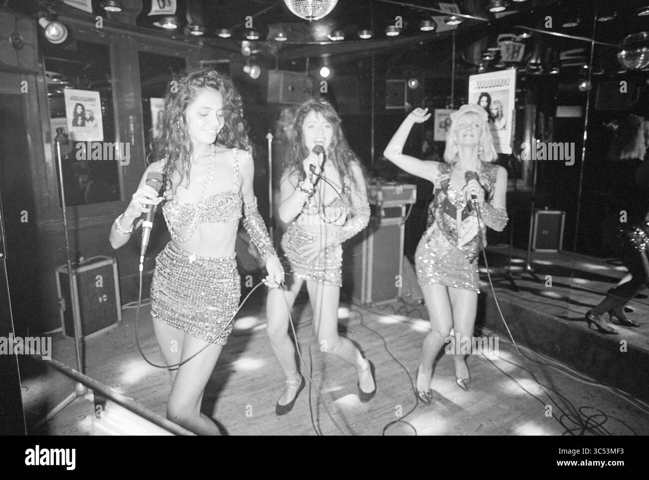 Barbarella dans les 3 Mousquetaires, musique, performance, 30-07-1989 Whizgle News, Dutch Desk, pays-Bas, 1950-2000 trois femmes vêtues de tenues étincelantes se produisent énergiquement, tenant des microphones et chantant passionnément sur scène. L'ambiance est animée, avec un éclairage vibrant et une boule disco reflétant une atmosphère ludique. Banque D'Images