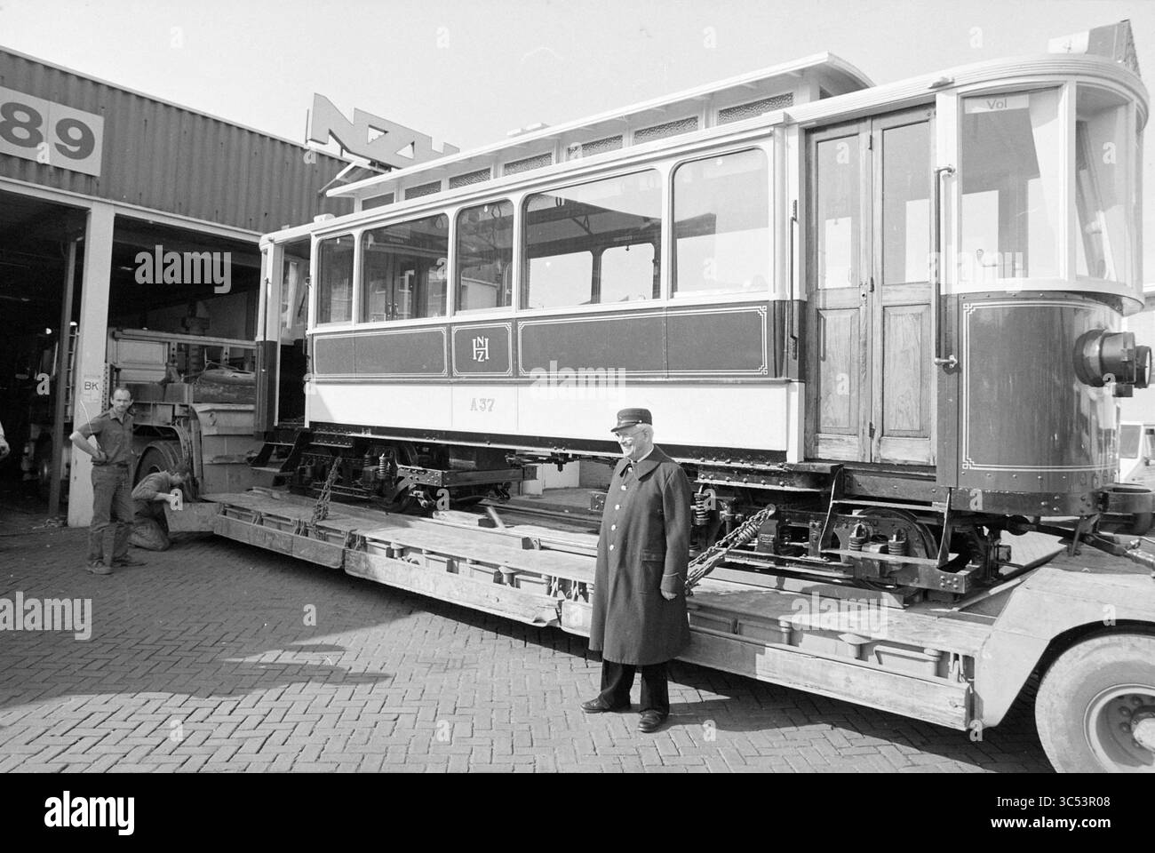 Arrivée de l'ancien tram, dépôt NZH Leidsevaart, Tram, Haarlem, Leidsevaart, pays-Bas, 31-03-1989 Whizgle News, Dutch Desk, pays-Bas, 1950-2000 Un tramway historique se tient sur un camion à plateau, avec un préposé en uniforme devant. En arrière-plan, les travailleurs sont vus engagés dans leurs tâches, faisant allusion à un environnement d'atelier animé. Le tramway, marqué du numéro 137, reflète un design classique, mettant en valeur le savoir-faire de son époque. Banque D'Images