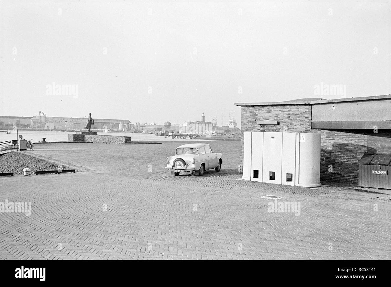 Toilettes à la tête du port d'IJmuiden, IJmuiden, pays-Bas, 14-01-1969 Whizgle News, Dutch Desk, pays-Bas, 1950-2000 Une voiture ancienne garée près d'un front de mer avec des bâtiments industriels et une statue en arrière-plan, montrant une scène calme le long d'une zone pavée. Banque D'Images