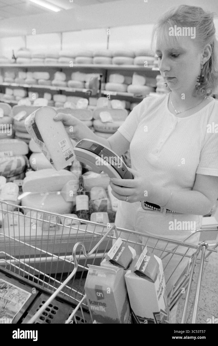 Lecteur de codes-barres AH, Heemstede, Heemstede, pays-Bas, 16-06-1994 Whizgle News, Dutch Desk, pays-Bas, 1950-2000 Une femme inspecte une meule de fromage tout en faisant ses courses dans un supermarché, tenant dans son autre main un scanner numérique de prix. Les étagères derrière elle sont remplies de divers produits de fromage et de cartons de lait, indiquant un environnement d'épicerie occupé. Banque D'Images