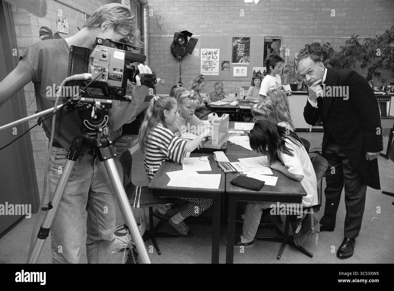Vidéo Pieter Vermeulen School, 22-06-1990 Whizgle News, Dutch Desk, pays-Bas, 1950-2000 Une scène de classe mettant en scène un groupe d'étudiants engagés dans diverses activités sur des bureaux, sous la supervision d'un enseignant. Au premier plan, une personne fait fonctionner une caméra vidéo, capturant les interactions des élèves, tandis qu'un autre adulte regarde attentivement. L'environnement est rempli de matériel éducatif et de décorations, créant une atmosphère d'apprentissage dynamique. Banque D'Images