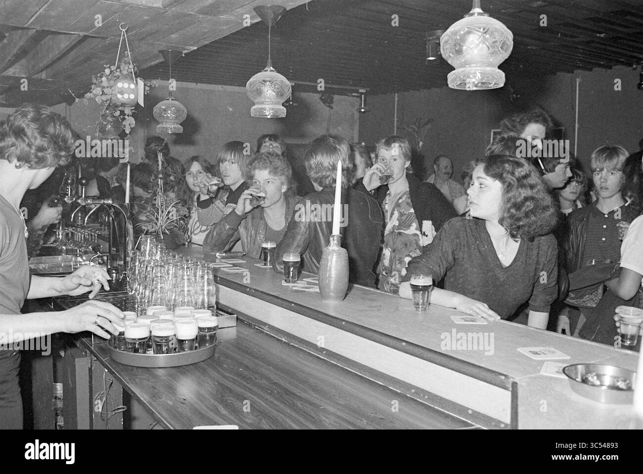 Ouverture du club de jeunes Seven Eleveven Beverwijk, quartiers, centres communautaires, magasins locaux, centres de formation, ouverture, ouvertures, mise en service, Beverwijk, pays-Bas, 16-04-1981 Whizgle News, Dutch Desk, pays-Bas, 1950-2000 Une scène de bar animée remplie d'un groupe diversifié de clients énergiques qui socialisent et apprécient leurs boissons. Le barman est occupé à servir, tandis que des groupes d'amis s'engagent dans la conversation, créant une atmosphère animée. Un éclairage décoratif et une variété de boissons rehaussent l'ambiance. Banque D'Images