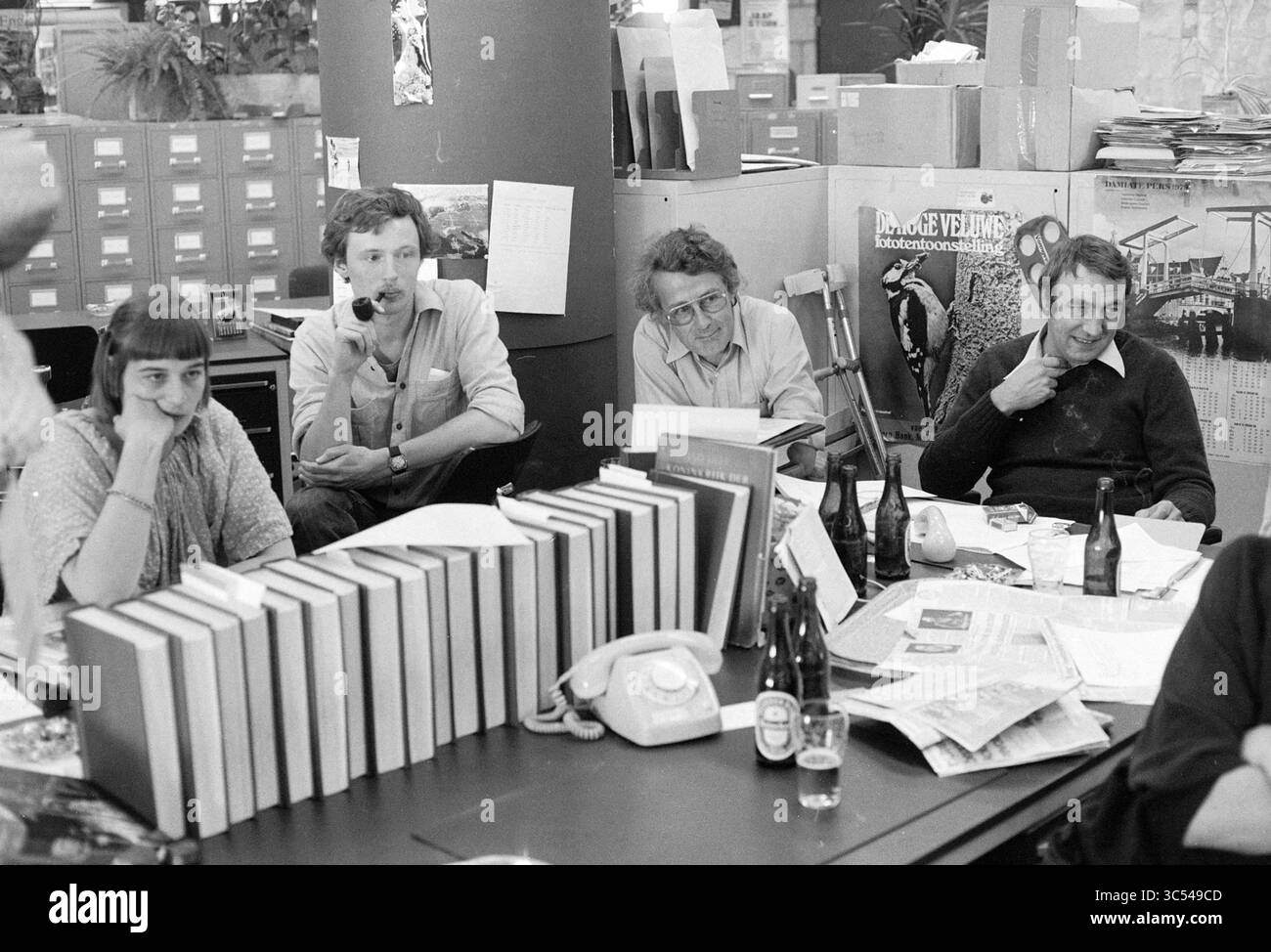 Équipe éditoriale HD à douze jeux provinciaux, Haarlems Dagblad, etc et IJmuider courant et Koeri, 19-05-1979 Whizgle News, Dutch Desk, pays-Bas, 1950-2000 Un groupe de quatre personnes s'assoit autour d'une table encombrée de livres, de papiers et de bouteilles, engagés dans des discussions. Ils présentent un mélange d'expressions, de la contemplation à la concentration, dans un environnement de bureau animé rempli de piles de fichiers et divers éléments en arrière-plan. Banque D'Images
