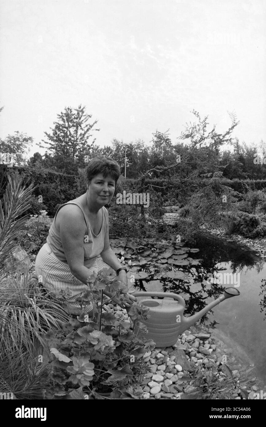 Garden Pride Heemstede et Vogelenzang, 09-06-1993 Whizgle News, Dutch Desk, pays-Bas, 1950-2000 Une femme est assise au bord d'un étang serein entouré d'une végétation luxuriante, s'occupant doucement de son jardin avec un arrosoir à la main. La scène tranquille reflète son lien avec la nature et son dévouement à nourrir ses plantes. Banque D'Images