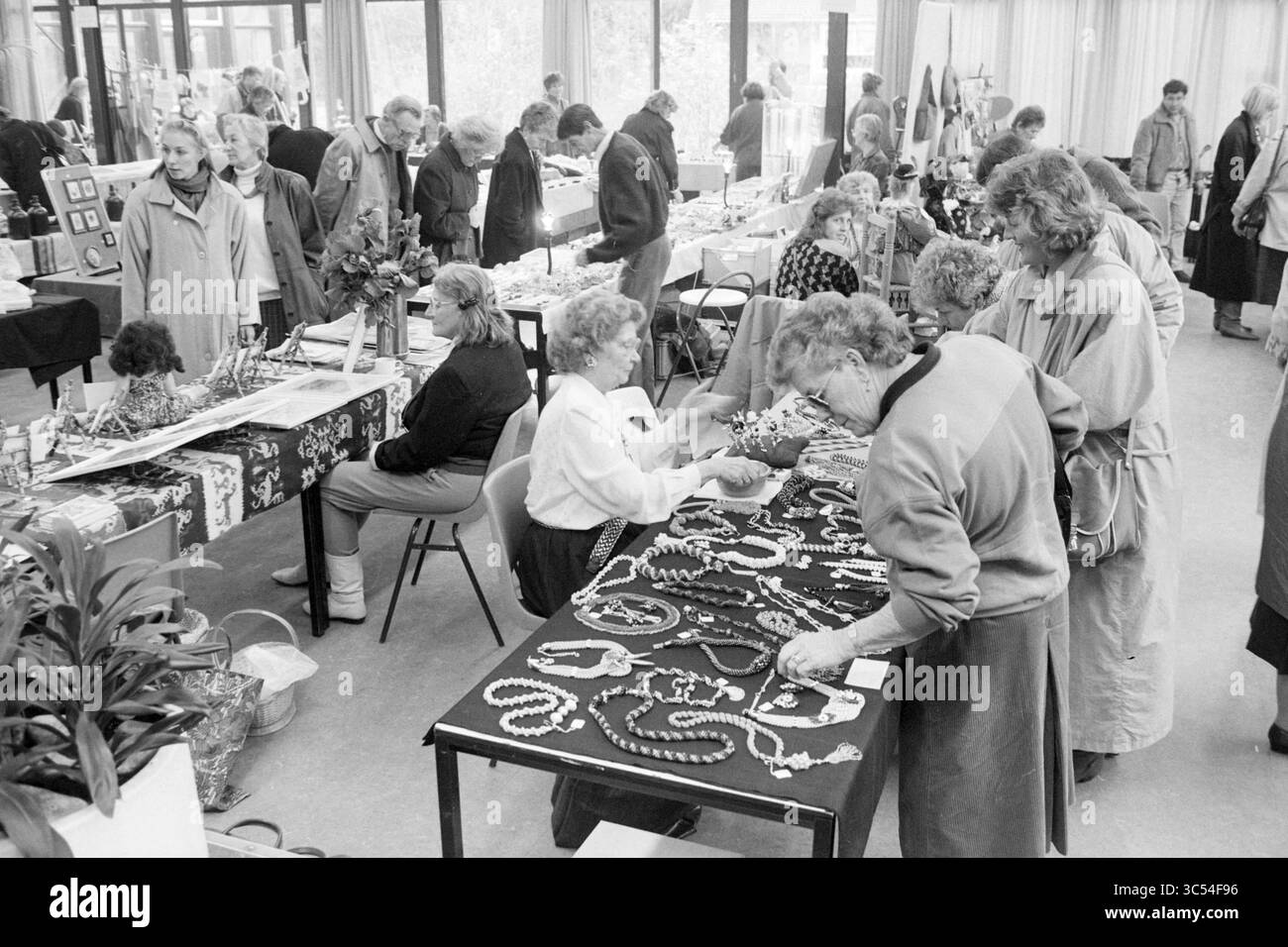 Gift Market, Santpoort, Market, Santpoort, 28-11-1987 Whizgle News, Dutch Desk, pays-Bas, 1950-2000 Une scène de marché intérieur animée où les vendeurs présentent une variété de bijoux faits à la main, attirant une foule diversifiée d'acheteurs. Les tables sont ornées de colliers et d'accessoires colorés, tandis que les participants s'engagent activement dans la navigation et les conversations. Banque D'Images