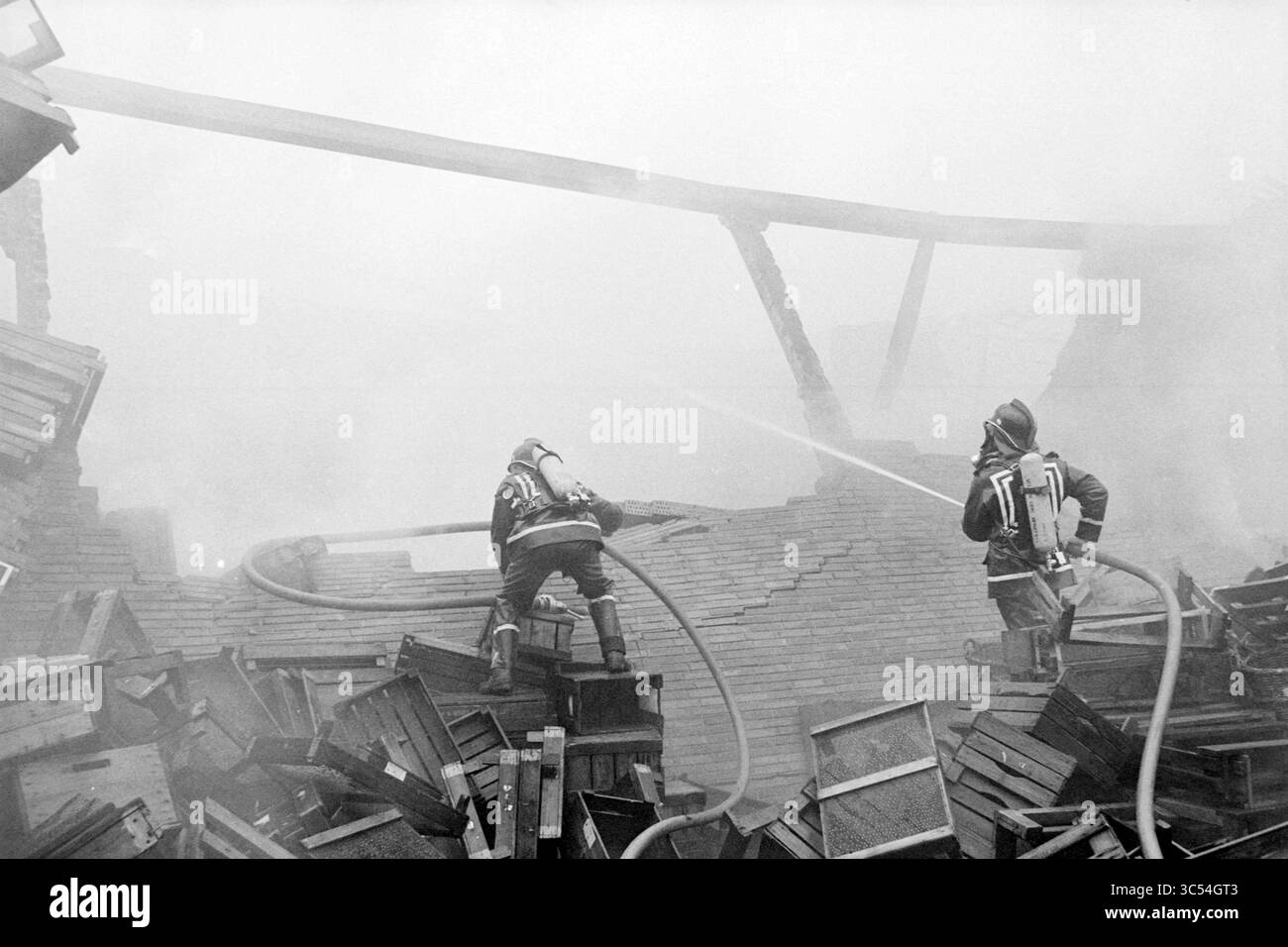 Hangar à ampoules à feu fa. Willemsen Hillegom, pompiers, Hillegom, 02-03-1980 Whizgle News, Dutch Desk, pays-Bas, 1950-2000 les pompiers combattent un incendie enflammé au milieu des débris, utilisant des tuyaux pour asperger les flammes tandis que de la fumée épaisse enveloppe la scène. Leur détermination précise souligne le courage et l'urgence de leur mission. Banque D'Images