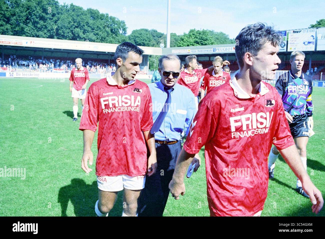 AZ - Telstar, 19-08-1995 Whizgle News, Dutch Desk, pays-Bas, 1950-2000 Un groupe de joueurs de football en maillots rouges avec « FRISIA FINANCIERING » sur la marche avant du terrain, paraissant concentré et déterminé. Ils sont accompagnés par un homme en chemise bleue, probablement un entraîneur ou un officiel de l'équipe, alors qu'ils se dirigent vers les lignes de touche après un match. Le stade est rempli de spectateurs en arrière-plan. Banque D'Images