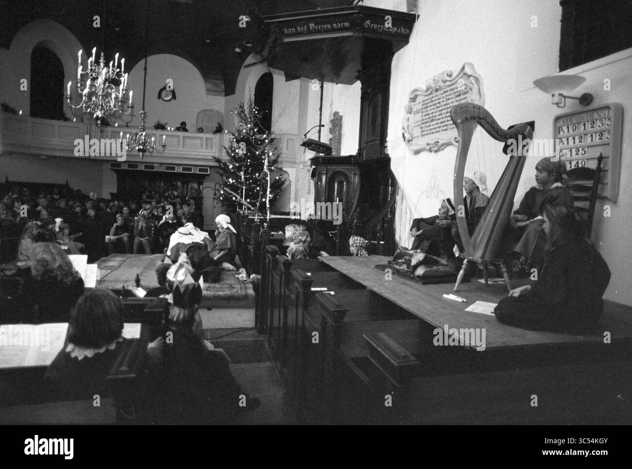 Pièce de Noël pour enfants, Église réformée, Bloemendaal, Bloemendaal, 19-12-1992 Whizgle News, Dutch Desk, pays-Bas, 1950-2000 scène festive dans une église, où des musiciens se produisent devant un public réuni pour célébrer. Un harpiste joue tandis qu'un sapin de Noël joliment décoré ajoute à l'atmosphère de vacances. Les interprètes sont habillés en tenue traditionnelle, améliorant le sentiment d'occasion. Banque D'Images