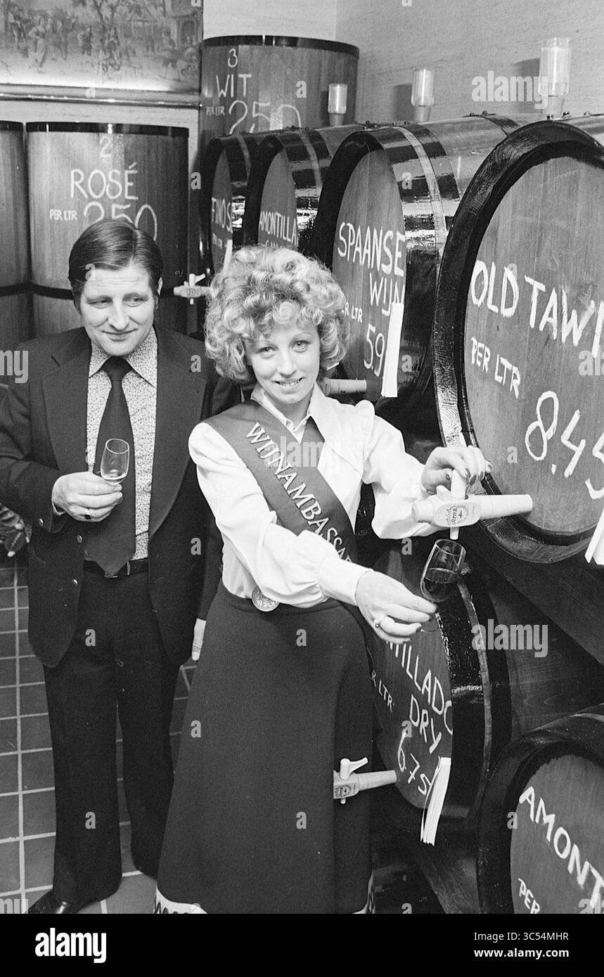 Ouverture de la cave Hillegom, ouverture, ouvertures, mise en service, 13-03-1975 Whizgle News, Dutch Desk, pays-Bas, 1950-2000 Un homme et une femme sont engagés dans une dégustation de vin dans une cave à vin, la femme vêtue d'une tenue habillée et tenant un verre, tout en souriant. Les fûts de bois derrière eux affichent différents types de vin et prix, créant une atmosphère chaleureuse et accueillante axée sur l'appréciation du vin. Banque D'Images
