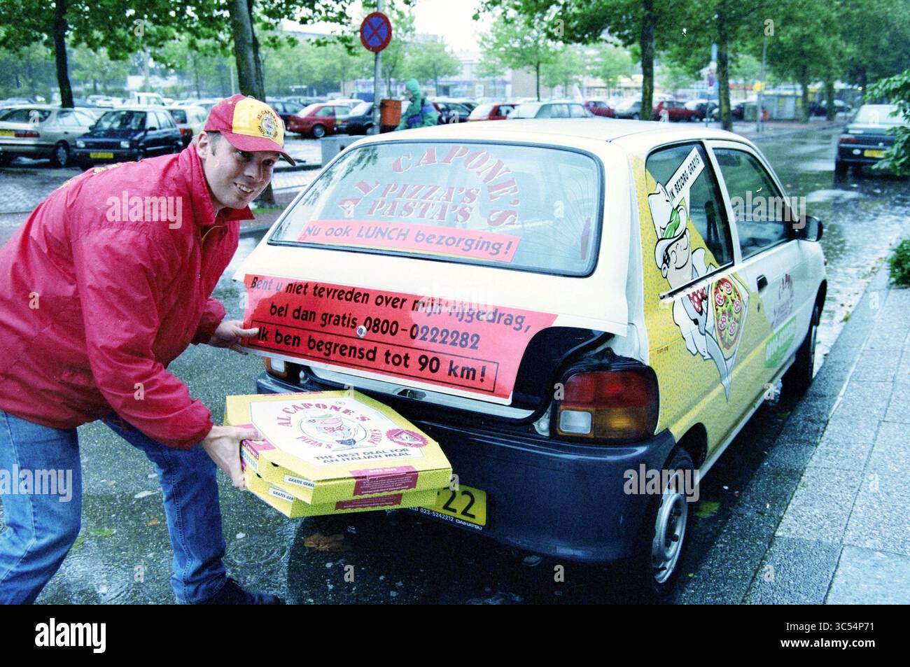Livraison de pizza Al Capone, 13-09-1998 Whizgle News, Dutch Desk, pays-Bas, 1950-2000 Un livreur tient de grandes boîtes de pizza tout en se tenant debout à côté d'une voiture de livraison de pizza colorée ornée de publicité. La scène met en scène une rue de la ville avec de la verdure et des notes de temps humide. Banque D'Images Livraison de pizza Al Capone, 13-09-1998 Whizgle News, Dutch Desk, pays-Bas, 1950-2000 Un livreur tient de grandes boîtes de pizza tout en se tenant debout à côté d'une voiture de livraison de pizza colorée ornée de publicité. La scène met en scène une rue de la ville avec de la verdure et des notes de temps humide. Banque D'Images