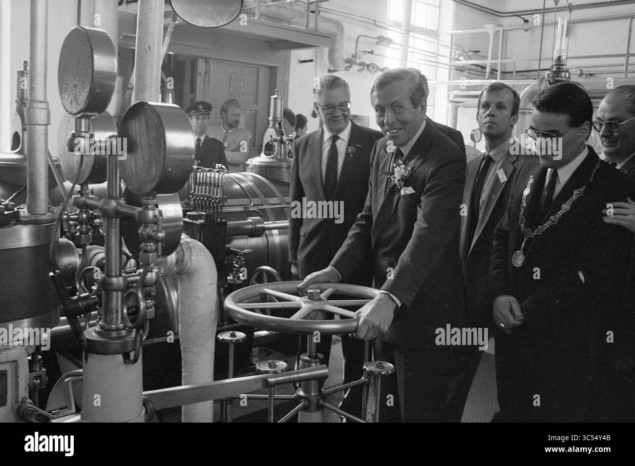 Ouverture de la station de pompage de vapeur à mi-chemin de Prince Claus, ouverture, ouvertures, mise en service, station de pompage de vapeur et station de pompage de vapeur, Halfweg, 10-06-1987 Whizgle News, Dutch Desk, pays-Bas, 1950-2000 Un groupe d'hommes habillés se réunit autour d'une grande machine industrielle, un homme souriant lorsqu'il interagit avec le panneau de commande, suggérant un moment de célébration ou de démonstration. L'atmosphère transmet un sentiment d'innovation et de progrès, avec diverses composantes mécaniques en vue. Banque D'Images