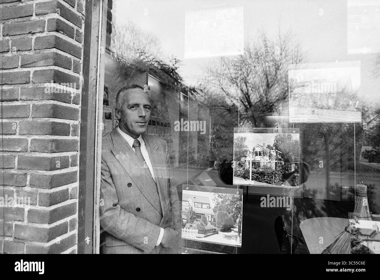 Agent immobilier, Hoofddorp, pays-Bas, 21-10-1993 Whizgle News, Dutch Desk, pays-Bas, 1950-2000 Un homme en costume se tient réfléchi près d'une fenêtre, encadrée par un mur de briques, tandis qu'il regarde dehors. Derrière lui, diverses photographies de maisons sont exposées, laissant entrevoir un lien possible avec l’immobilier ou l’architecture. La scène reflète un moment de contemplation et de professionnalisme. Banque D'Images
