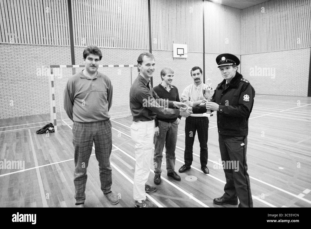 1er prix tournoi de football en salle Beverwijk, football en salle, Beverwijk, pays-Bas, 02-01-1987 Whizgle News, Dutch Desk, pays-Bas, 1950-2000 Un groupe de cinq hommes se tient debout dans une salle de sport, un homme en uniforme présentant fièrement un trophée à un autre. Les autres regardent, s'engagent et soutiennent, alors qu'ils participent à un moment de célébration. Le cadre comprend un poteau de but et un plancher en bois, ajoutant à l'ambiance sportive. Banque D'Images