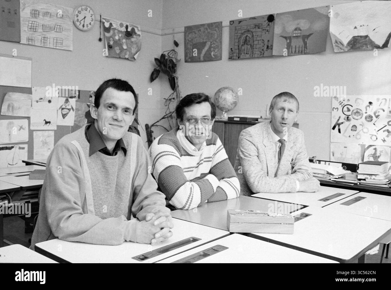 Fusion scolaire, Lijnden, Ecoles, Lijnden, 18-04-1984 Whizgle News, Dutch Desk, pays-Bas, 1950-2000 trois hommes sont assis à une table de classe, souriant et interagissant les uns avec les autres. Derrière eux, des œuvres d'art colorées pour enfants décorent les murs, mettant en valeur un environnement d'apprentissage créatif et dynamique. Banque D'Images